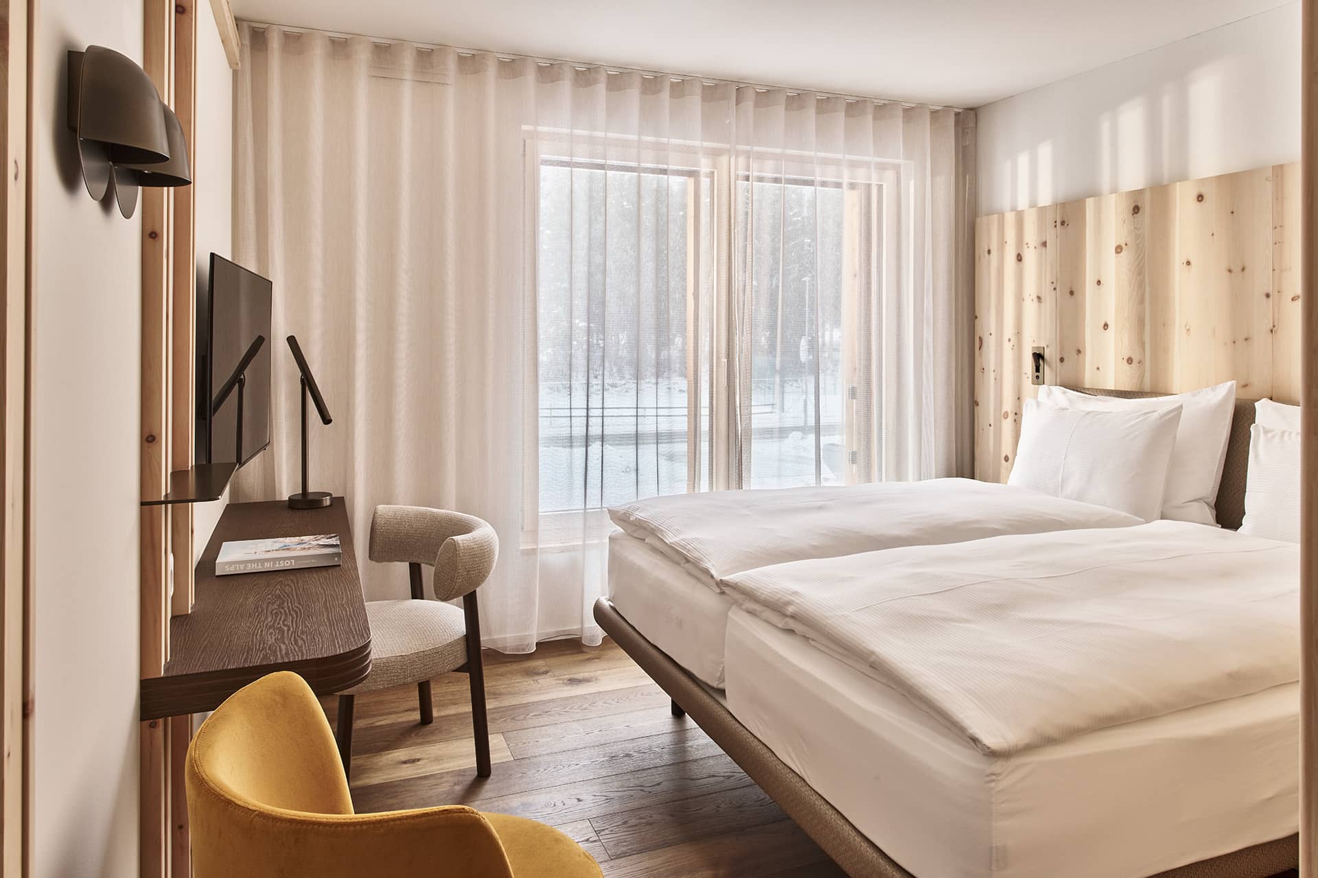 Schlafzimmer im Apartment mit Doppelbett, Holzwand, Schreibtisch, Sessel und bodentiefen Fenstern