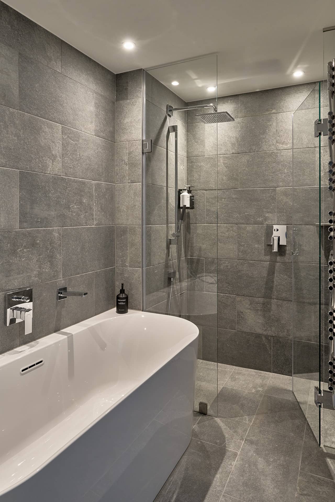 Modernes Badezimmer mit freistehender Badewanne, begehbarer Dusche, grauen Steinfliesen und Glasabtrennung