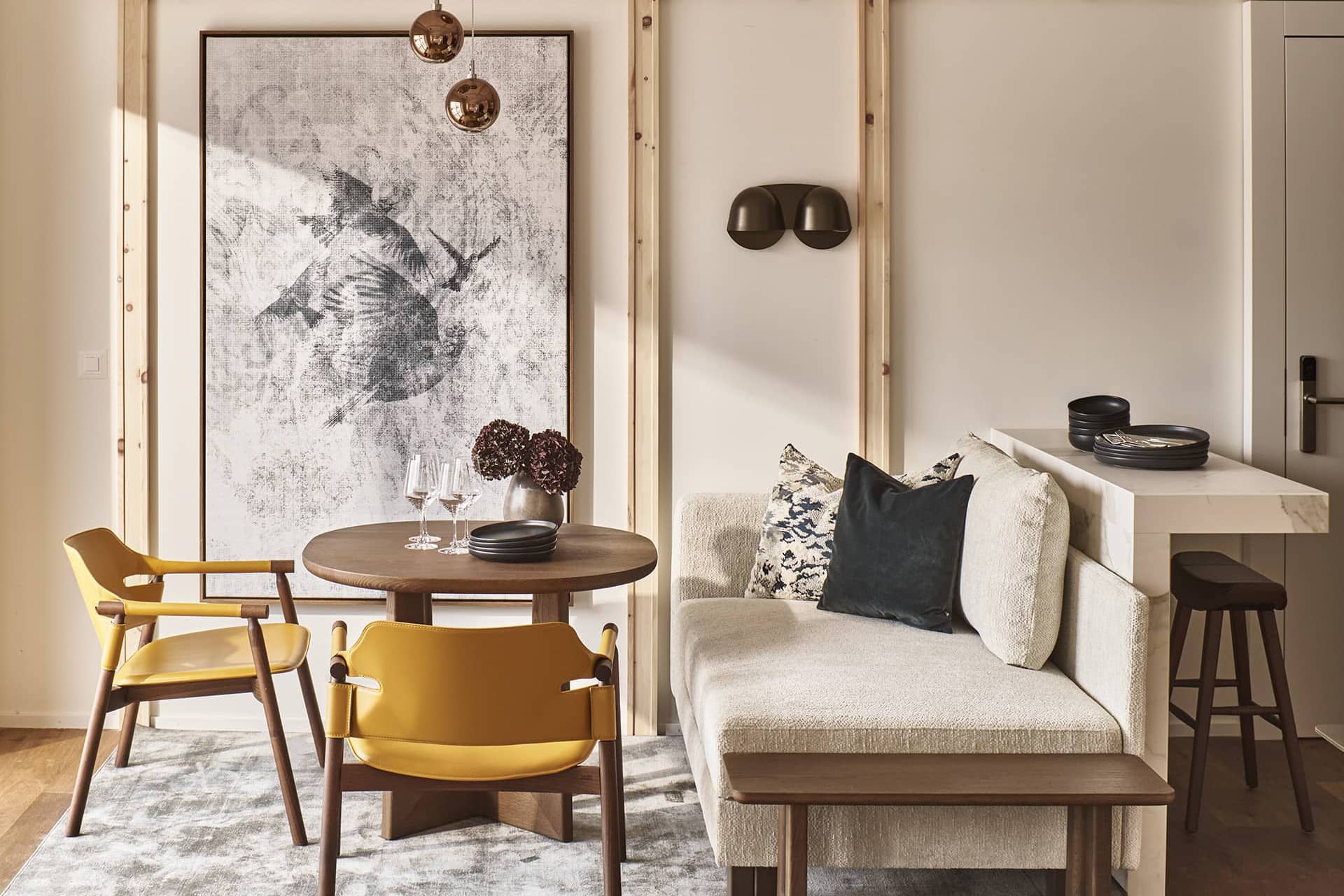 Wohn- und Essbereich der Apartment Suite mit rundem Holztisch, gelben Stühlen, gemütlicher Sitzbank und großem Kunstwerk an der Wand