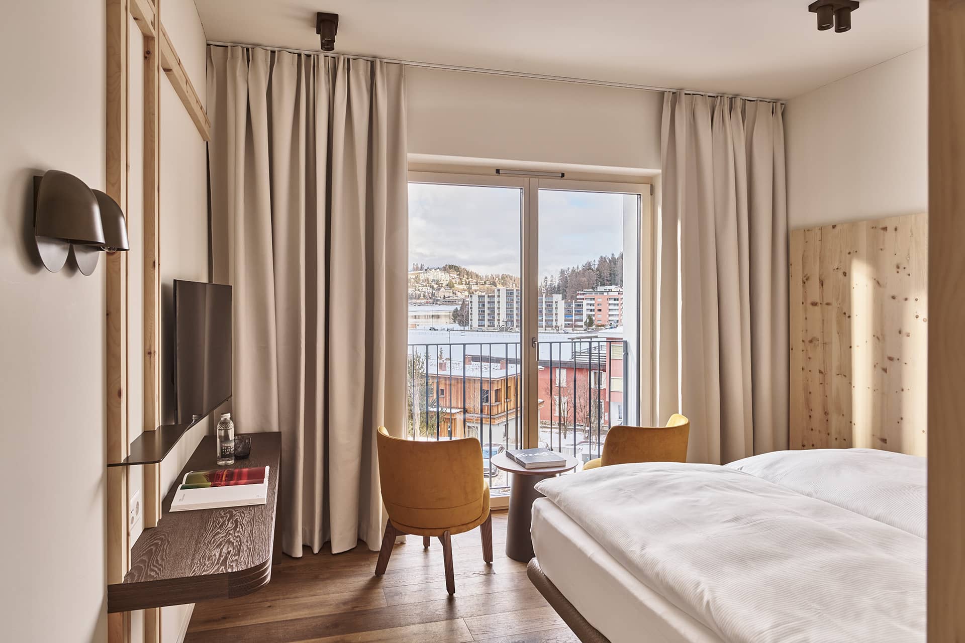 Schlafzimmer der Apartment Suite mit großem Doppelbett, Holzrückwand, bodentiefen Fenstern und warmem Tageslicht