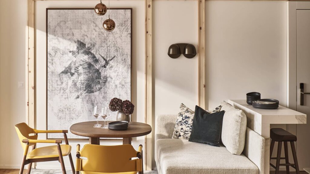 Wohn- und Essbereich der Apartment Suite mit rundem Holztisch, gelben Stühlen, gemütlicher Sitzbank und großem Kunstwerk an der Wand