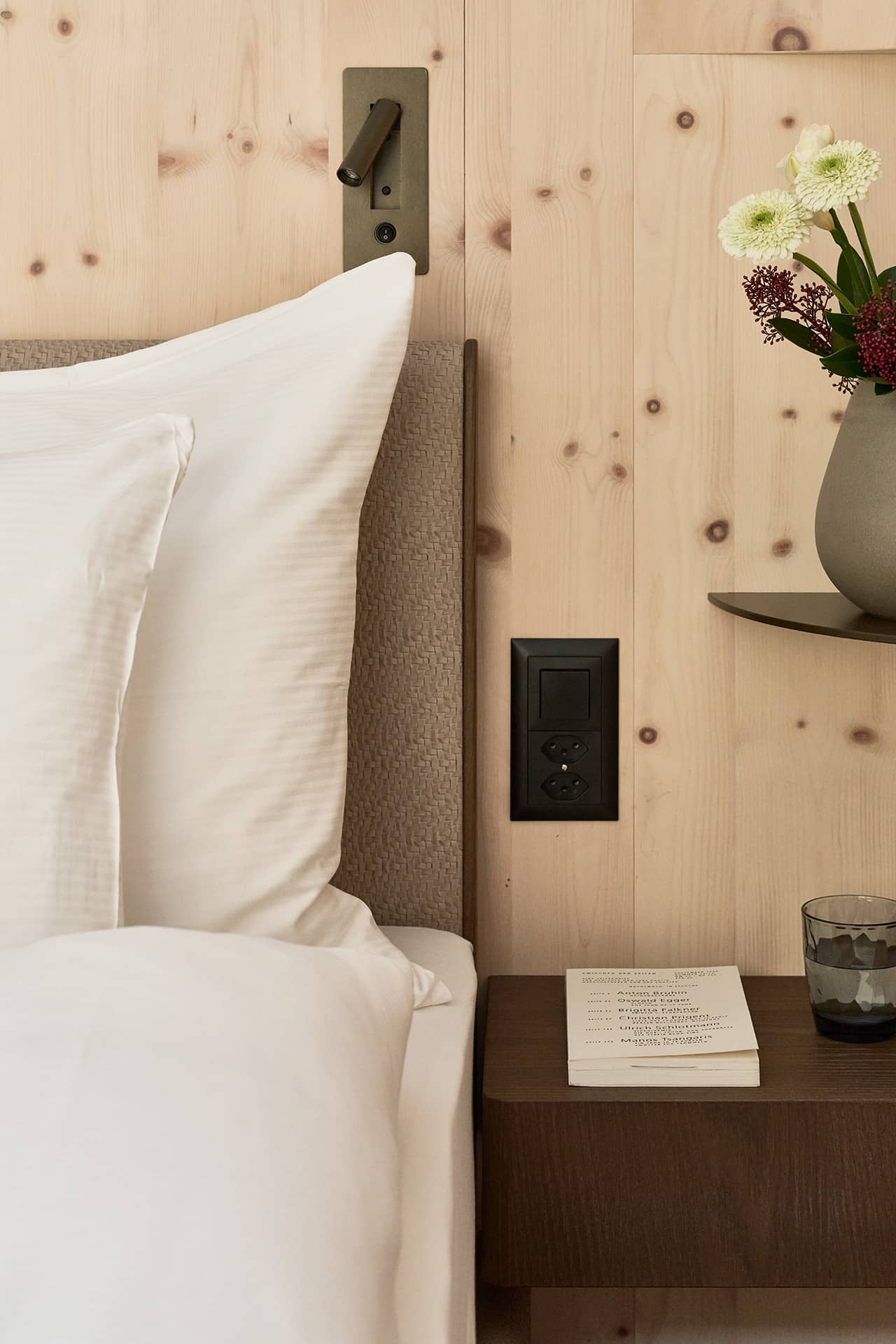 Detailansicht des Bettes in der Suite 2 mit Holzwand, Leselampe und Nachttisch