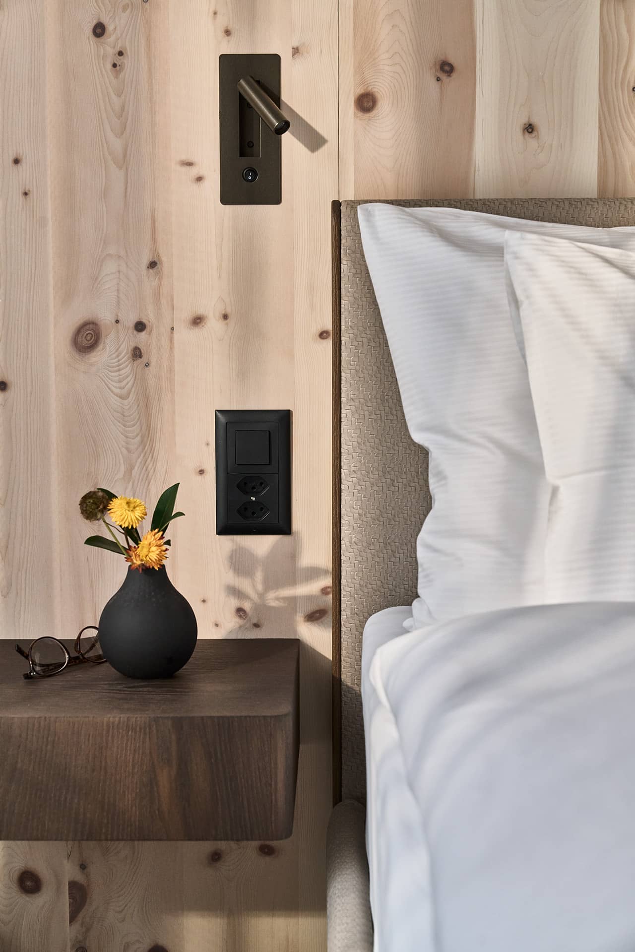 Detail im Schlafbereich der Suite mit Nachttisch, Leselampe und Holzwand