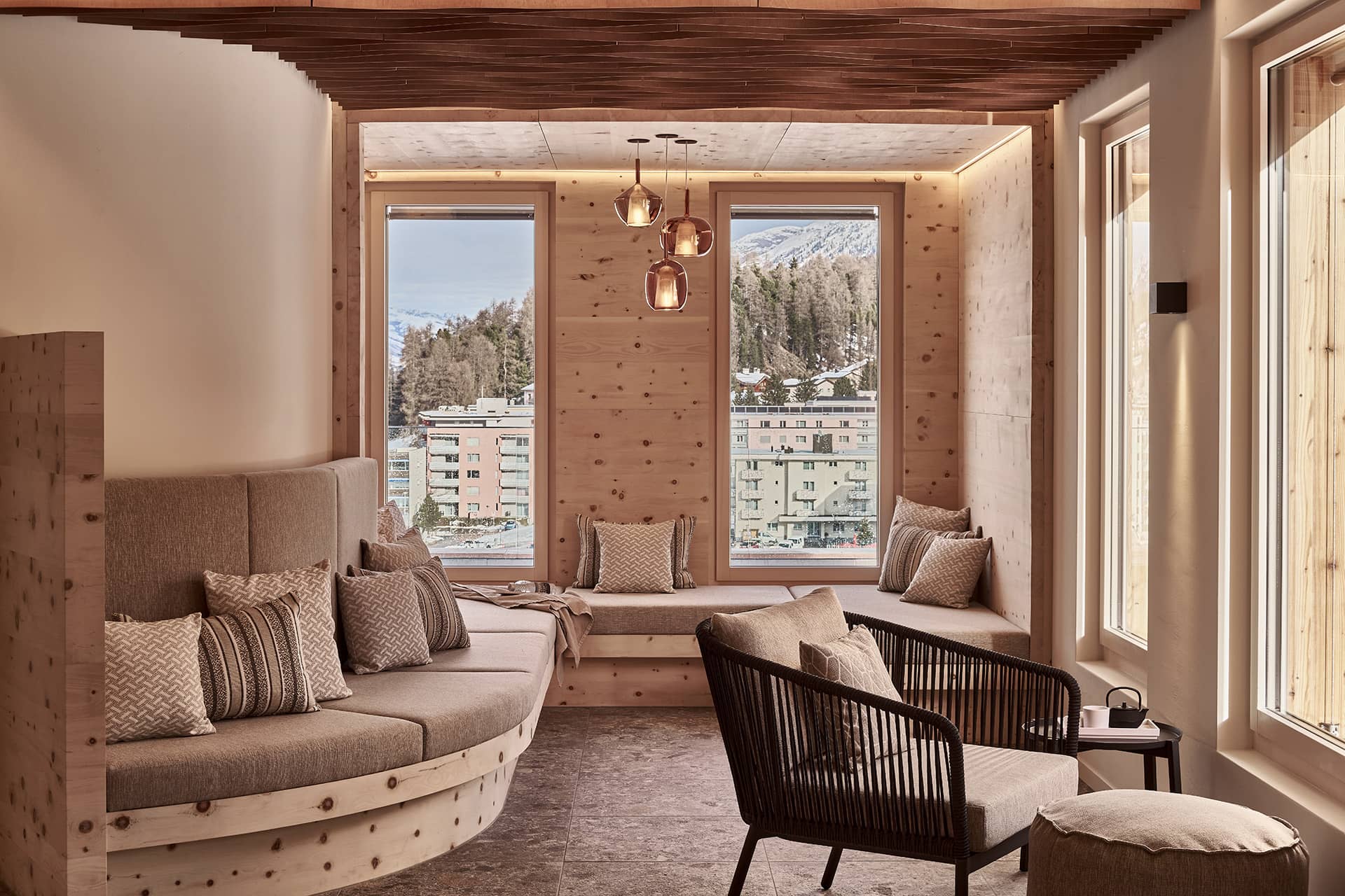 Ruhebereich im Spa mit geschwungenen Sitznischen aus Holz, großen Fenstern und Blick auf die Berge