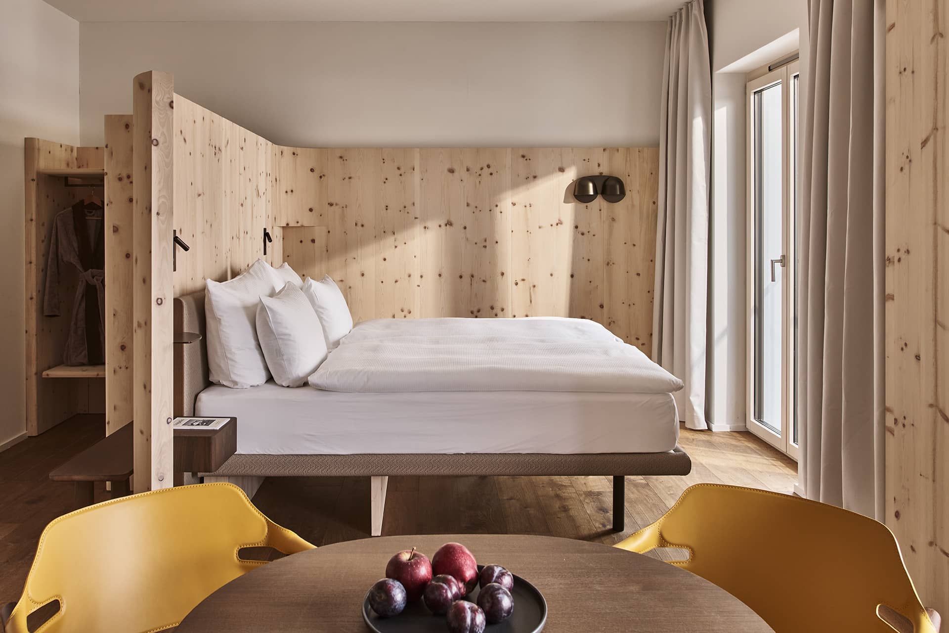 Modernes Loft mit großem Doppelbett, heller Holzverkleidung und minimalistischem Design im warmen Tageslicht.